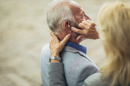 Senior couple with a hearing problem sitting on bench outdoorの写真素材