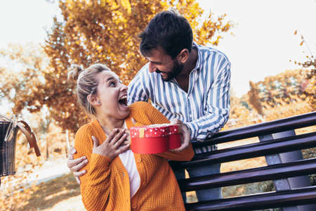 Man surprises woman with a gift in the park.の写真素材
