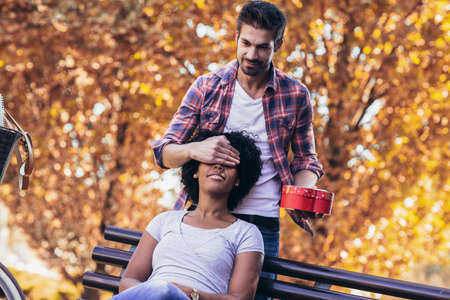 Man surprises woman with a gift in the park.の写真素材