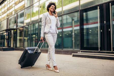 Portrait of excited young business woman using smart phone with travel bagの写真素材