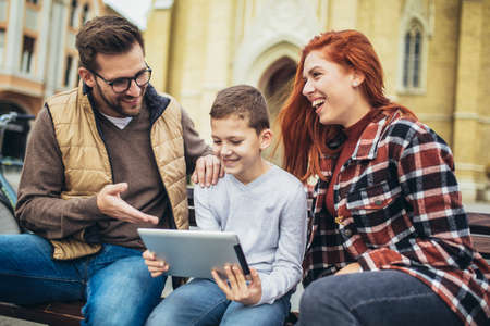 Family sitting on bench, relaxing using gadget, browsing internet.の写真素材