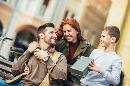 Young family with present outdoor.Mother and son giving a gift box to father.の写真素材