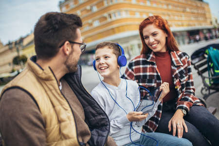 Family sitting on bench, relaxing using gadget, browsing internet.の写真素材