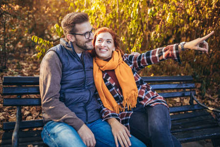 Beautiful young couple sitting on a bench in the autumn parkの写真素材