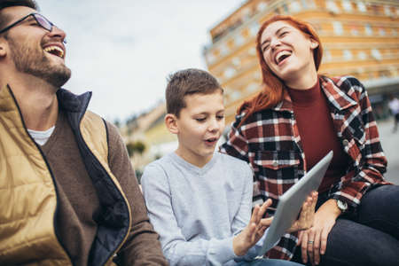 Family sitting on bench, relaxing using gadget, browsing internet.の写真素材