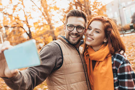 Happy couple in autumn park make selfie photo.の写真素材