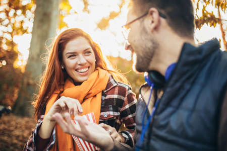 Beautiful young couple sitting on a bench in the autumn park eating popcorn.の写真素材