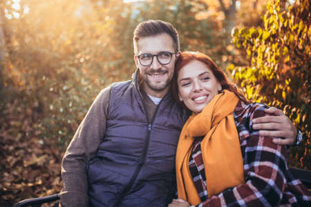 Beautiful young couple sitting on a bench in the autumn parkの写真素材