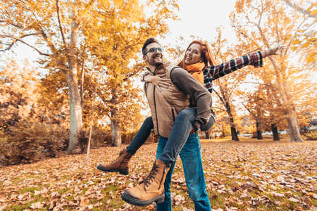 Smiling man carrying woman piggyback in autumn park.の写真素材