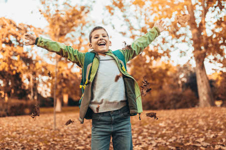 Happy joyful school kid with backpack having fun in autumn parkの写真素材