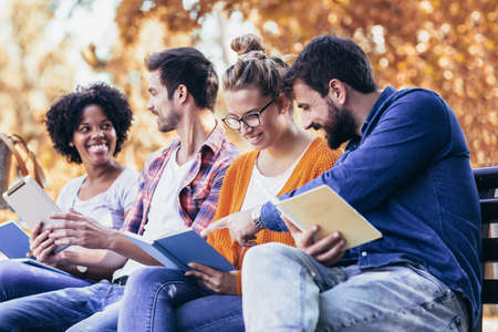 Students talking sitting on bench outdoors in park after university classes.の写真素材