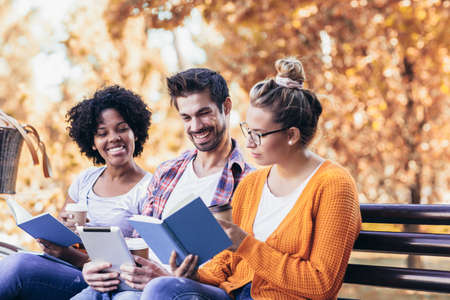 Students talking sitting on bench outdoors in park after university classes.の写真素材