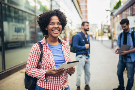 Young african woman holding books while standing on background of university and friends.の写真素材