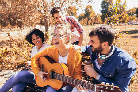 Group of young people hangout in the park.They sitting on bench ,singing and playing guitar.の写真素材