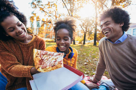 Mixed family having fun while picnicking in the park eating pizza.の写真素材