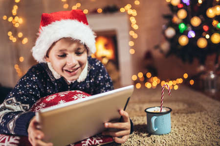 Cute little boy playing on tablet in front of a christmas treeの写真素材
