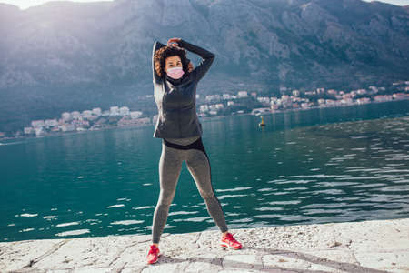 Athletic young woman with protective mask doing exercises on the beach