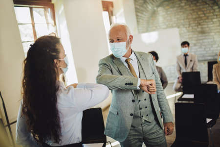 Business man and woman with safety masks greeting with elbow bump in office. Virus protection conceptの写真素材