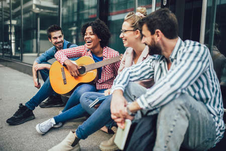 Group of young friends hangout in city.They are sitting,singing and playing guitar.の写真素材