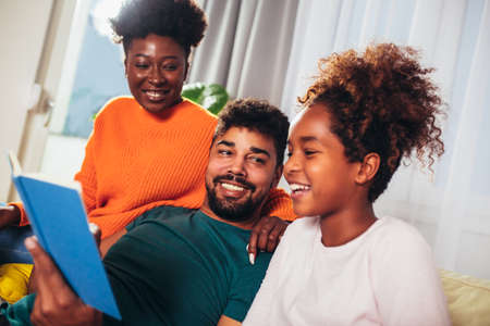 Happy african american family reading book together, staying at home during virus quarantine