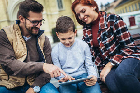 Family sitting on bench, relaxing using gadget, browsing internet.