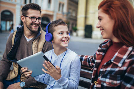 Family sitting on bench, relaxing using gadget, browsing internet.の写真素材