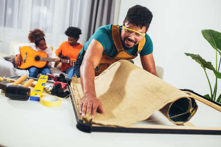 Craftsman working on frame for picture at home, when his daughter practicing guitar.の写真素材