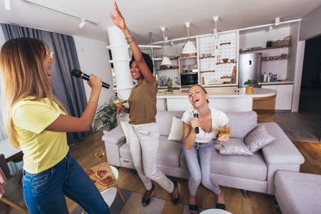 Young woman singing in to microphone at home party having fun. Bachelorette party, karaoke, music concert and holidays conceptの写真素材