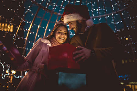 Young romantic couple holding gift box having fun outdoors in winter before Christmas.