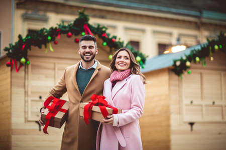 Young romantic couple holding gift box having fun outdoors in winter before Christmas.の写真素材