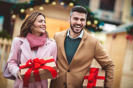 Young romantic couple holding gift box having fun outdoors in winter before Christmas.の写真素材