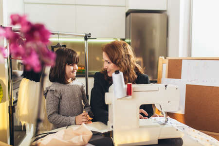 Cheerful young woman sewing with her daughter. She working at home.の写真素材