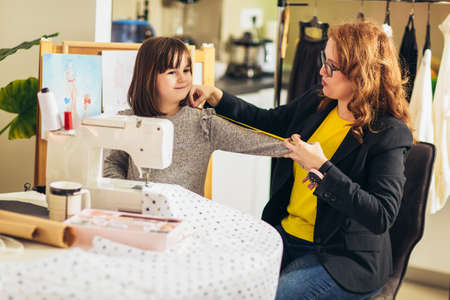 Cheerful young woman sewing with her daughter. She working at home.の写真素材