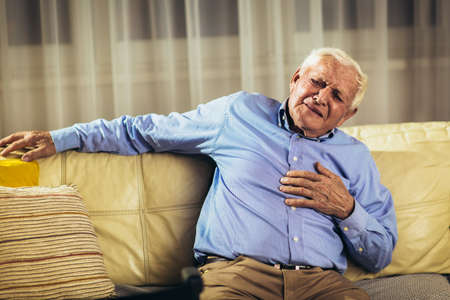 Senior man with chest pain suffering from heart attack at homeの写真素材