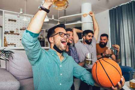 Happy male friends  wearing black face protective mask watching basketball at home