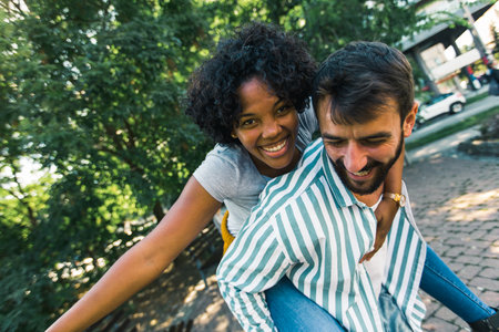 Young coupe in park. Boyfriend carrying his girlfriend on piggyback.