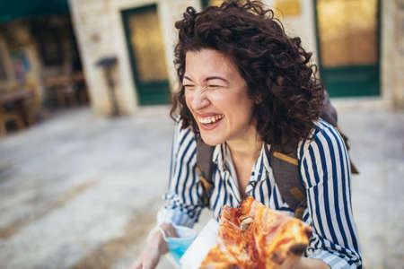 Beautiful young tourist woman eating a slice of pizza outdoorの写真素材