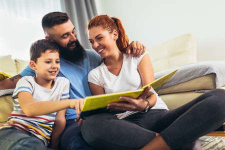 Happy family reading storybook at home in the living roomの写真素材