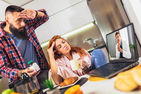 Young ill couple having medical teleconsultation using laptop at home.の写真素材