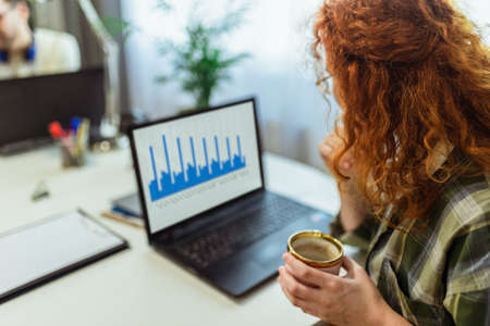 Remote work life. Young red-haired woman working on laptop at home.