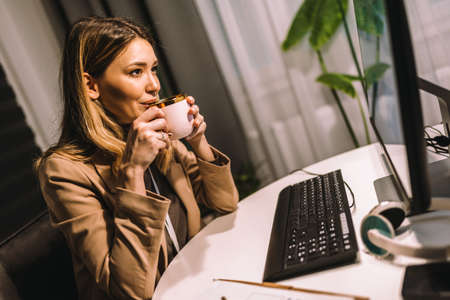 Beautiful woman working on a computer at the night at home, drink coffee.