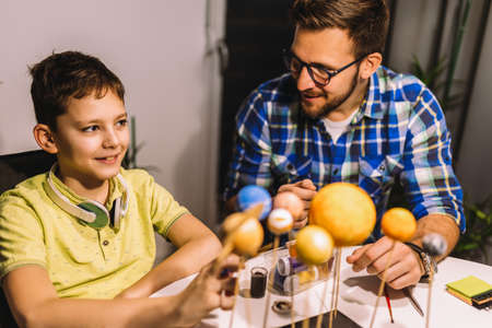 Happy school boy and his father making a solar system for a school science project at homeの写真素材