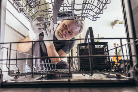 Portrait Of Male Technician Repairing Dishwasher In Kitchenの写真素材