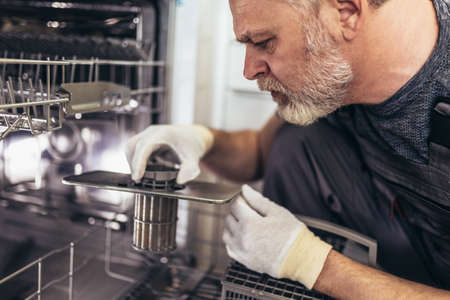 Portrait Of Male Technician Repairing Dishwasher In Kitchenの写真素材