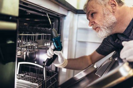 Man with toolbox repairing dishwasher in a household.の写真素材