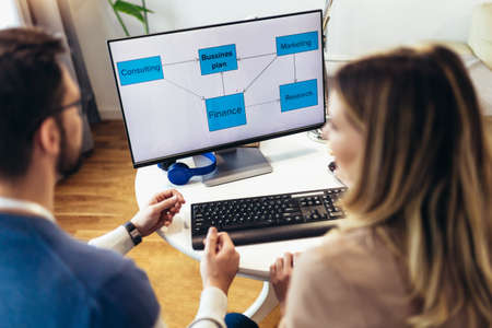 Successful young couple man and woman working on PC computer together while sitting at table at homeの写真素材