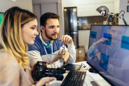 Young couple photographer and model sitting in front of computer and desk, looking to screen camera...