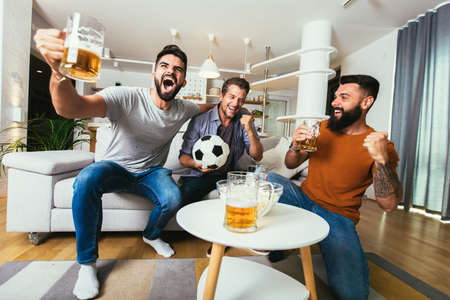 Excited friends watching football game and holding beer and popcornの写真素材