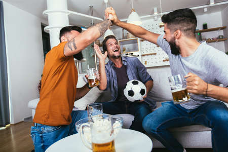 Excited friends watching football game and holding beer and popcorn