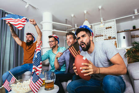 Friends cheering sport league together, holding rugby ball while watching championship.
